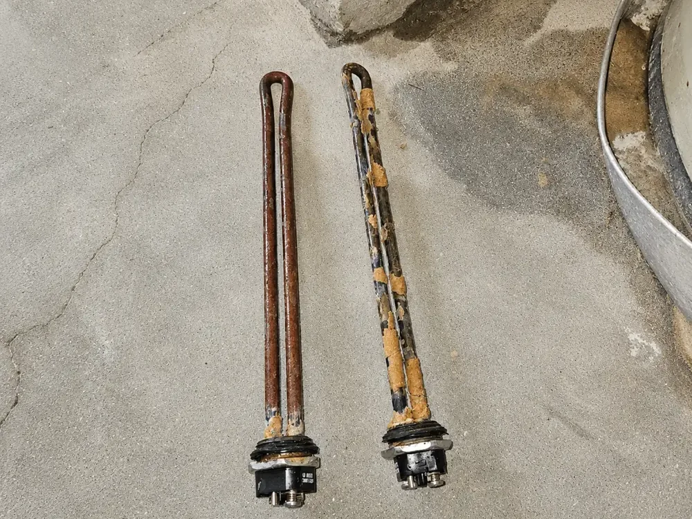 Two water heater heating elements removed during a replacement, one corroded and one heavily scaled with mineral buildup